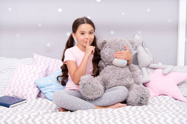 Girls secret. Cute kid show silence finger gesture. Little secret. Small girl play with teddy bear in bed. Keeping mouth shut. Being quiet. Silence and shushing. Top secret. Can you keep secret - Foto, Bild