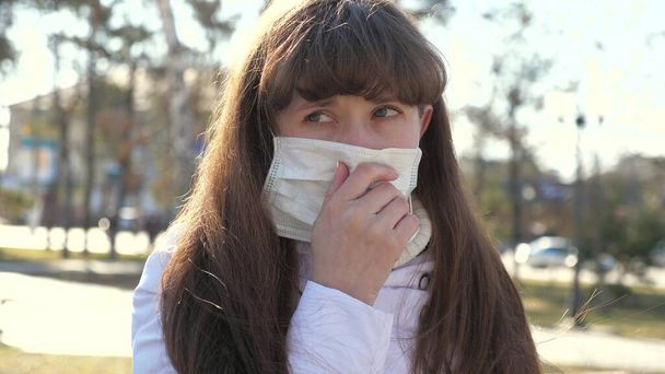 Mladá nemocná žena v ochranné masce kašle na ulici. Ta holka je nakažená kašlem. Nosič, Covid-19, koronavirus, symptom. Pandemický koronavirus. osoba s chřipkou. close-up - Fotografie, Obrázek