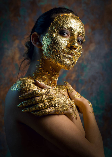 Fille avec un masque sur son visage en feuille d'or. Portrait en studio sombre d'une brune sur un fond abstrait. - Photo, image