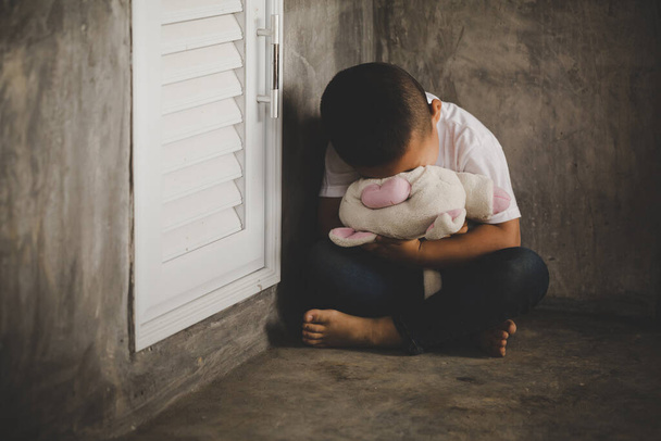 Dramatyczny portret małego chłopca siedzącego na podłodze i przytulającego pluszowego misia, Nieszczęśliwe dziecko siedzącego samotnie i patrzącego z niepokojącą twarzą, siedzącego chłopca na rogu kary. - Zdjęcie, obraz