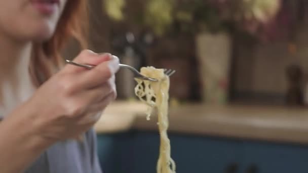Attractive redhead girl eats instant noodles with a fork in the kitchen. Eats junk food from a plastic box. Bad lifestyle. Food on the go. Woman Eating Asian wok Noodle from Take away Box. - Кадры, видео