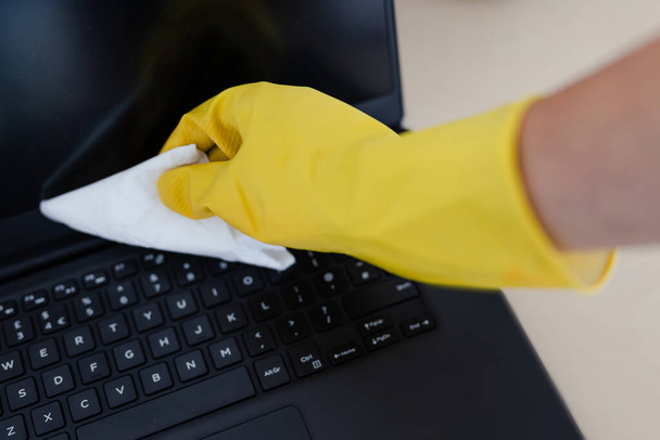 practice good hygiene against viruses and bacteria, hand with cleaning gloves disinfecting laptop keyboard with wipe - Foto, Imagen