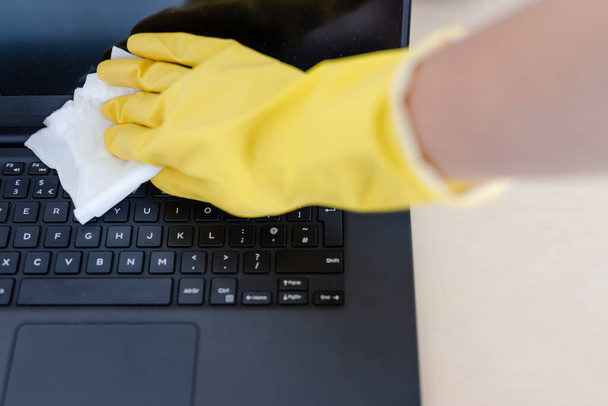 practice good hygiene against viruses and bacteria, hand with cleaning gloves disinfecting laptop keyboard with wipe - Photo, Image
