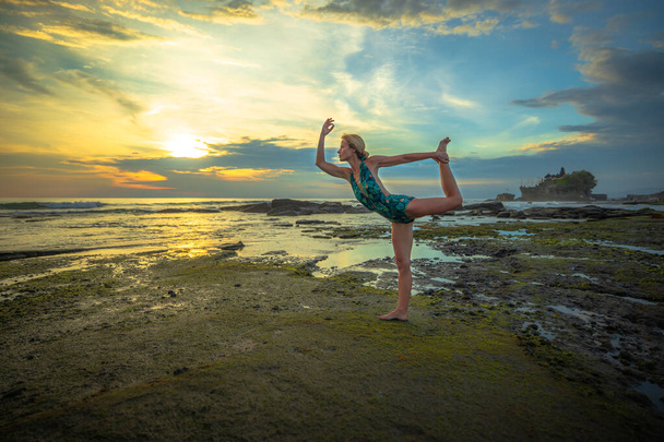Yoga al aire libre atardecer. Mujer atractiva practicando yoga, de pie en Natarajasana, Señor de la Posa de la Danza. Equilibrio, espalda doblando asana. Bali, Indonesia
 - Foto, imagen