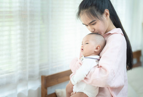 gelukkig mooi jong aziatisch moeder glimlachen knuffelen houden pasgeboren baby in haar armen thuis. Moeders dag banner met kopieerruimte voor reclame - Foto, afbeelding