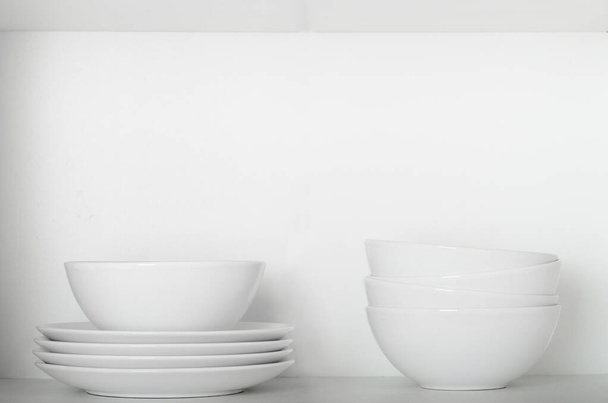 Білі тарілки і миски на полиці в шафі. Кухонне приладдя, чистий посуд
. - Фото, зображення