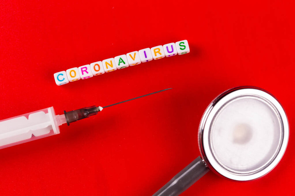 Pandemic and virus concept - Coronavirus text with syringe and phonendoscope on red background. Novel coronavirus Covid-19. - Fotografie, Obrázek