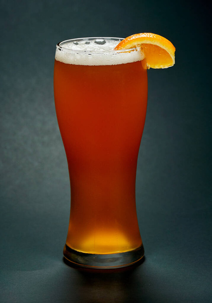 Vaso de cerveza roja con rodaja de naranja sobre fondo negro. La cerveza es una de las bebidas alcohólicas más antiguas, populares y consumidas en el mundo.
. - Foto, imagen