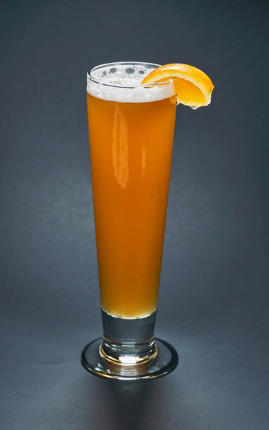 Un vaso alto de cerveza blanca sin filtrar con un trozo de naranja sobre un fondo negro. La cerveza es una de las bebidas alcohólicas más antiguas, populares y consumidas en el mundo.
. - Foto, imagen