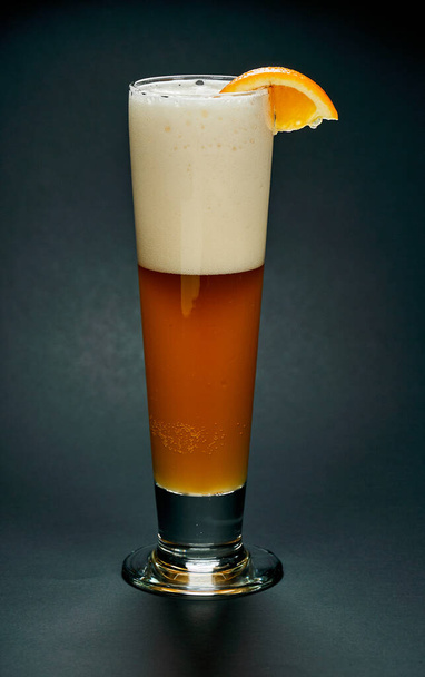 Un vaso alto de cerveza roja con un trozo de naranja sobre un fondo negro. La cerveza es una de las bebidas alcohólicas más antiguas, populares y consumidas en el mundo.
. - Foto, imagen