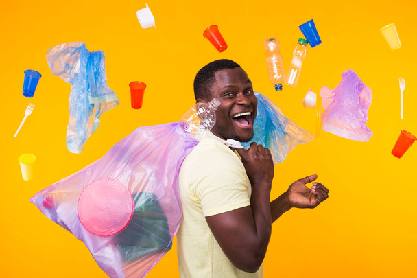 Probleem van afval, plastic recycling, vervuiling en milieu concept - grappige man dragen vuilniszak op gele achtergrond - Foto, afbeelding