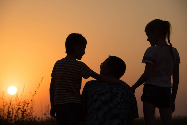 Vader en kinderen spelen in het park bij zonsondergang. Mensen hebben plezier op het veld. Begrip vriendelijk gezin en zomervakantie. - Foto, afbeelding