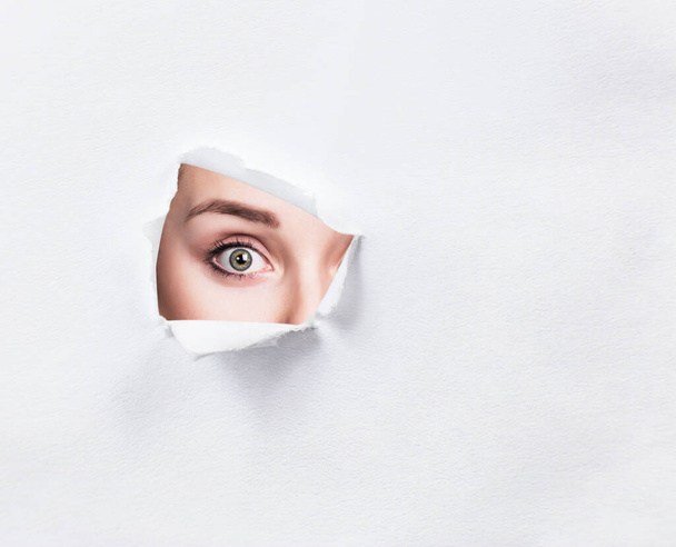 Surprised woman peeps into the slit of white paper. - Φωτογραφία, εικόνα