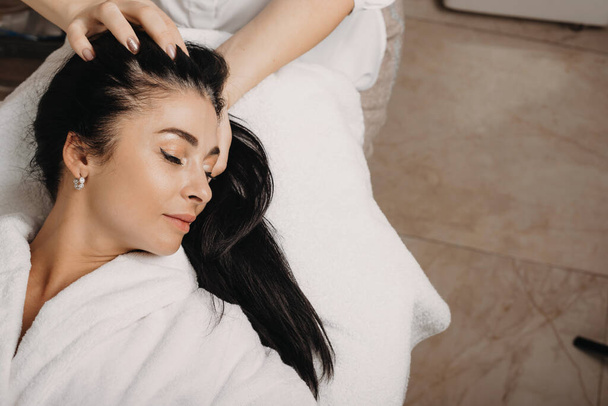 Bruna donna caucasica sdraiata sul divano con gli occhi chiusi durante un massaggio alla testa al salone
 - Foto, immagini