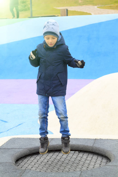 boy in warm clothes jumping on trampoline on modern playground outdoors - Foto, afbeelding