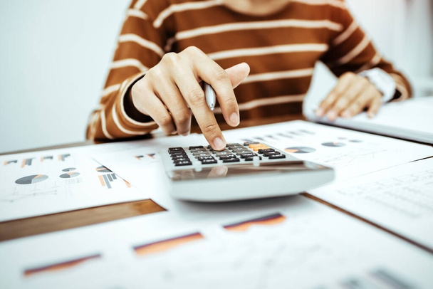 Молодая женщина предприниматель, работающая с бумагой и с помощью калькулятора для расчета финансовых расходов дома в гостиной за столом
. - Фото, изображение