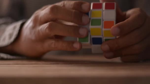 Egy üzletember közeledik, aki Rubik kocka rejtvényét oldja meg az asztalon. Problémamegoldás a munkahelyen koncepció. - Felvétel, videó