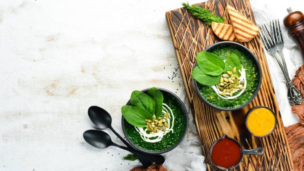 Green Spinach cream soup with cream and pumpkin seeds in a black bowl. Healthy food. Top view. Rustic style. - Foto, imagen