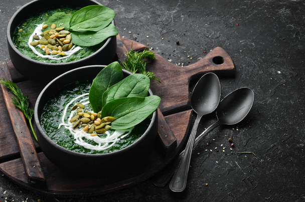 Green Spinach cream soup with cream and pumpkin seeds in a black bowl. Healthy food. Top view. Rustic style. - Фото, изображение