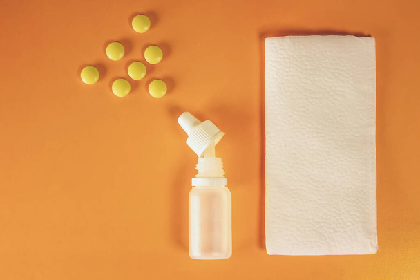 Witte plastic neusspray met tabletten en papieren zakdoeken op oranje achtergrond - sinusitis, geniantritis, rhinitis en andere ziekten van Ent-organen. Het concept van de behandeling van ziekten van de neus en - Foto, afbeelding