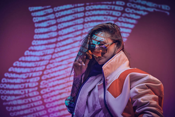 Tinta fêmea atraente posando em um néon luzes vívidas de um estúdio com texto, olhando confiante
 - Foto, Imagem