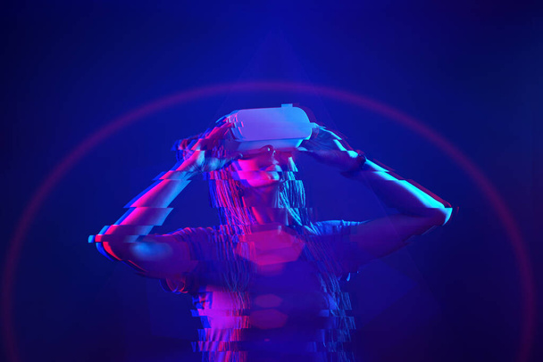 Woman is using virtual reality headset. Neon light studio portrait. Image with glitch effect. - Fotografie, Obrázek