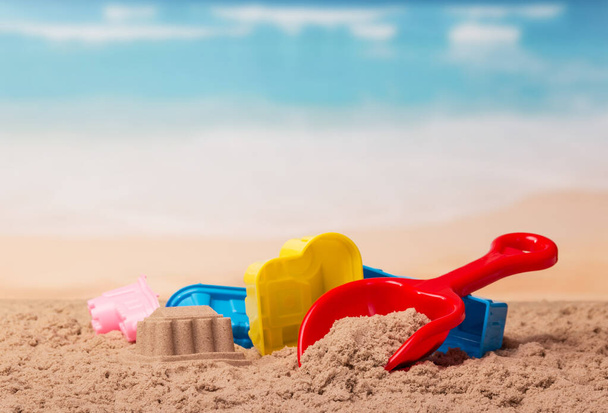 Helder plastic speelgoed en een zandkasteel in het zand tegen de zee. - Foto, afbeelding