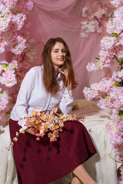 Genç kız yatak odasında çiçeklerle süslenmiş bir yatakta oturuyor. - Fotoğraf, Görsel