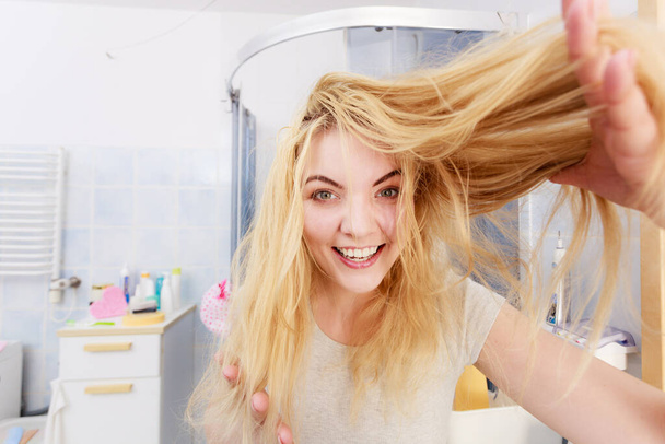 Onnellinen nainen, jolla on pitkät vaaleat hiukset. Positiivinen naaras suihkun jälkeen tuntuu puhtaalta ja näyttää kampauksensa ilolla
 - Valokuva, kuva