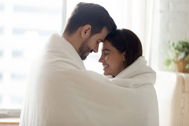 Happy loving couple wrapped in warm blanket touching foreheads - Фото, зображення