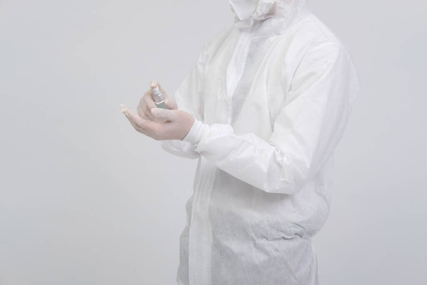 врач в биологической защитной униформе костюм одежды, маски, перчатки с ручной дозатор спирта для обеззараживания бактерий вируса
 - Фото, изображение