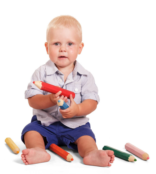 Cute little boy siedzi i trzyma duże ołówki izolowane na białym tle. - Zdjęcie, obraz