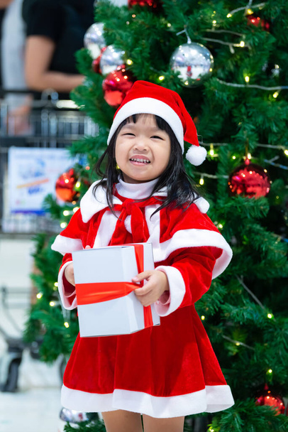 Portrait of cute asian little girl wear santa dress happy near christmas tree - Foto, imagen