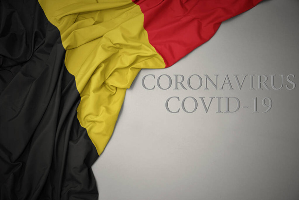 Üzerinde Coronavirus covid-19 yazan gri bir arka planda renkli bir Belçika bayrağı sallıyordu. konsept. - Fotoğraf, Görsel