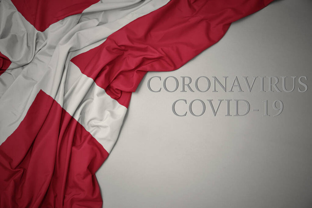 размахивая красочным национальным флагом денмарка на сером фоне с текстом coronavirus covid-19. концепция
. - Фото, изображение