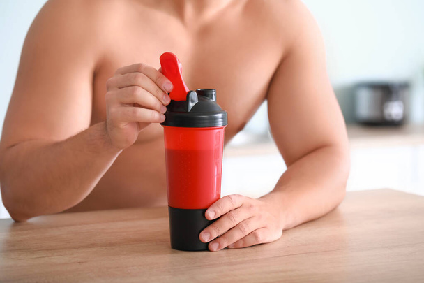 Sporty man with protein shake at home, closeup - Photo, Image