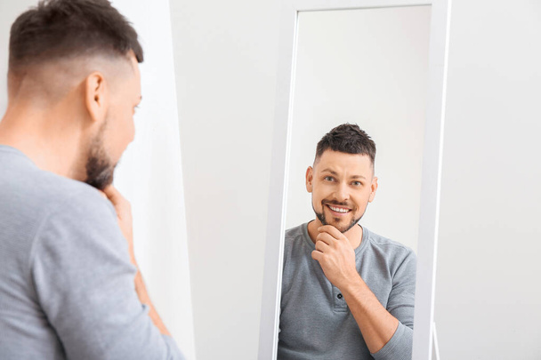 Handsome man looking in mirror at home - Фото, изображение
