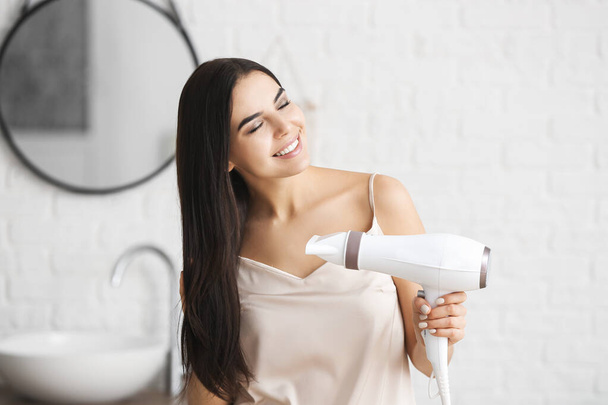 Beautiful young woman with hair dryer in bathroom - Fotografie, Obrázek