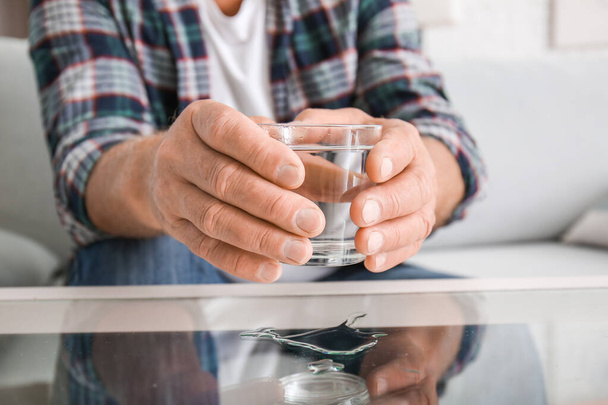 Hombre mayor con síndrome de Parkinson tomando un vaso de agua de la mesa, primer plano
 - Foto, Imagen