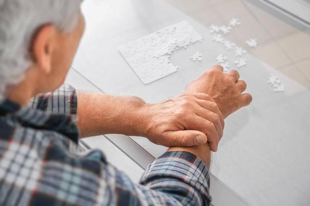 Старший мужчина с синдромом Паркинсона собирает головоломки дома
 - Фото, изображение