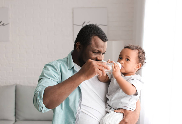 African-American man giving water to his cute baby at home - Fotó, kép