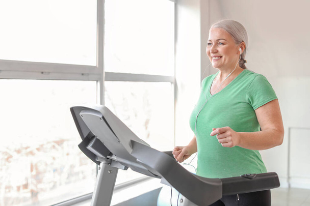 Sporty mature woman on treadmill in gym - Фото, изображение