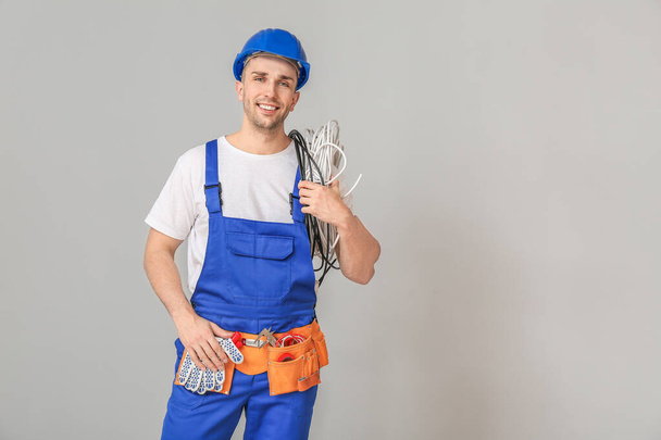 Handsome male worker with cables on grey background - Photo, Image