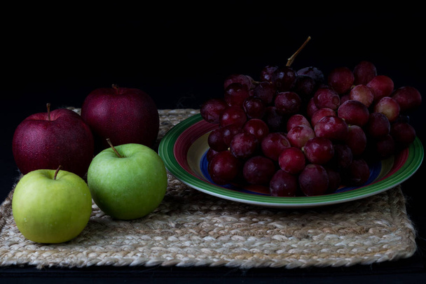 Uvas y manzanas en plato colorido con fondo negro  - Foto, Bild