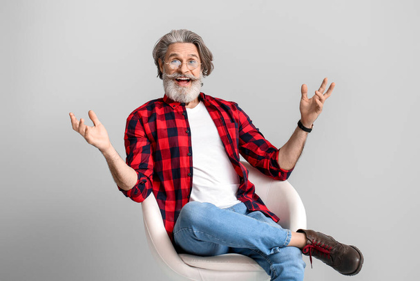 Feliz anciano sentado en sillón sobre fondo gris
 - Foto, Imagen