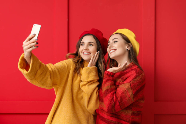 Young women in warm sweaters taking selfie on color background - Photo, Image
