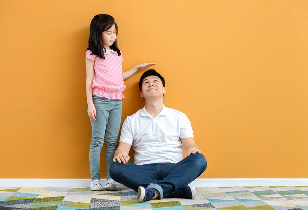 Азійська дівчинка, що вимірює висоту свого батька біля кольорової стіни. - Фото, зображення