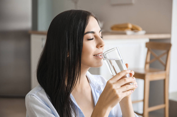 Beautiful young woman drinking water in kitchen - Photo, Image