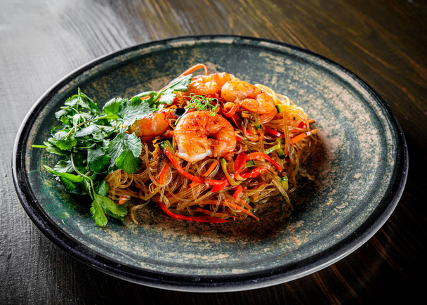 Stir fry noodles with vegetables and shrimps in plate on wooden table background - Foto, Imagem