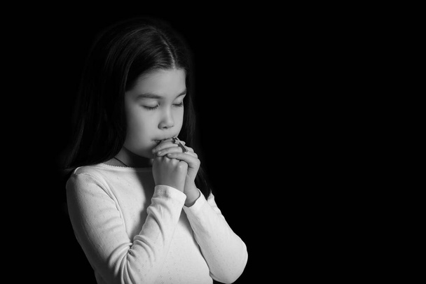 zwart en wit portret van schattig klein aziatisch meisje bidden op donkere achtergrond - Foto, afbeelding